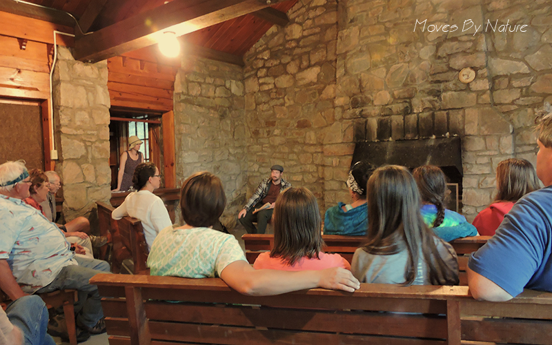 A group of people is seated in an old building watching a themed presentation